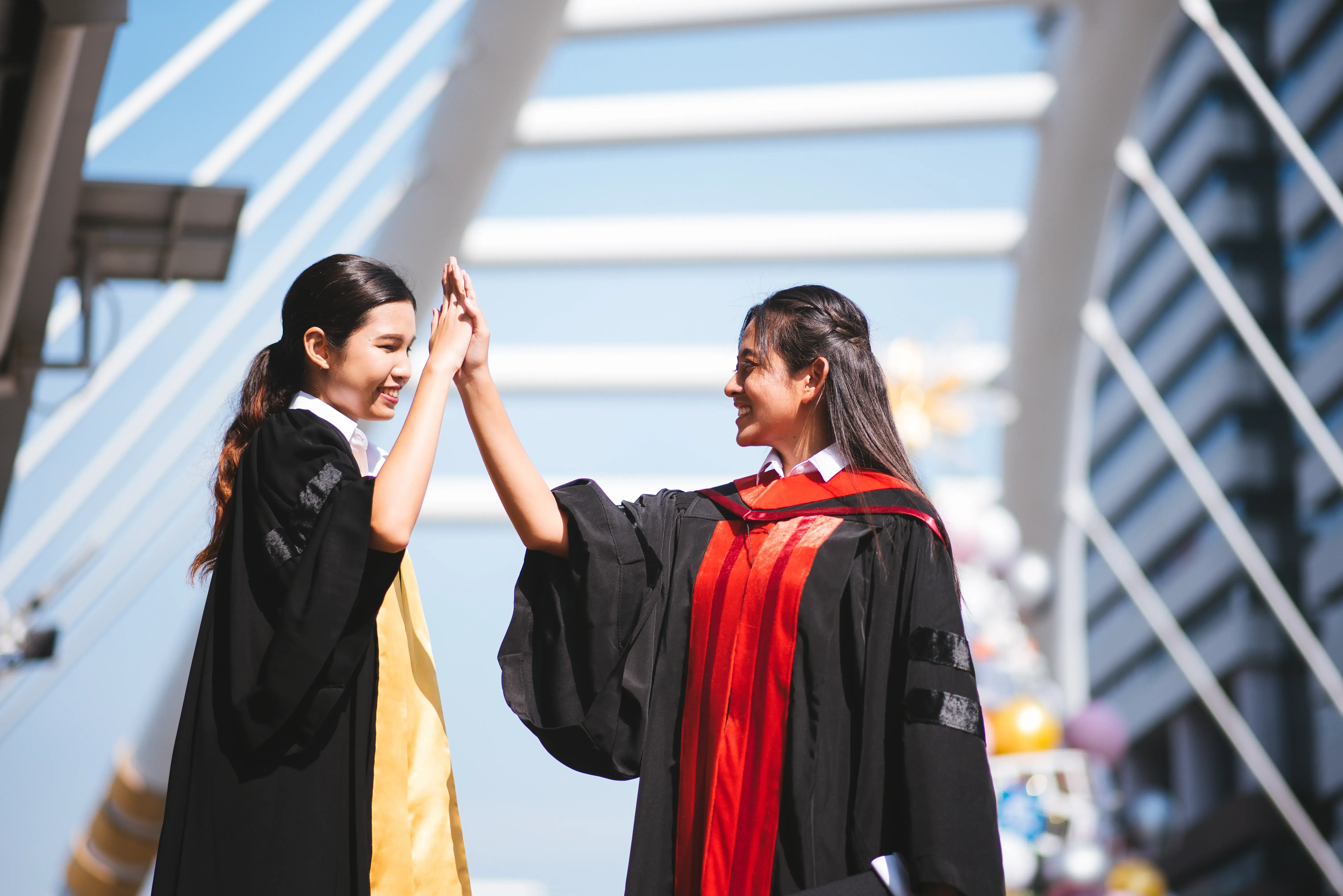 Two graduates in academic gowns giving each other a high five